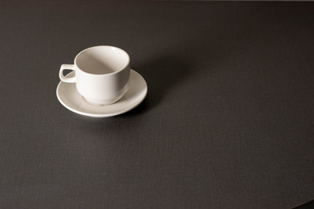 An empty white coffee cup and saucer, resting on a dark surface.