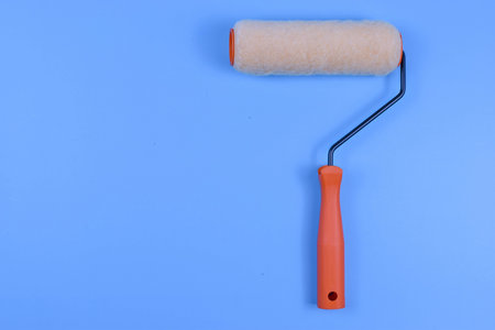 Paint roller with orange handle on blue background represents efficient surface coverage, commonly...