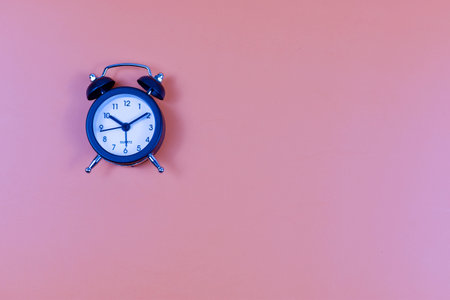 Analog alarm clock on pink background emphasizes time awareness, punctuality, and the visual impact of minimalist design.の写真素材