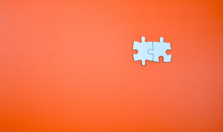Two interlocked white puzzle pieces on orange background, symbolizing connection, unity, or...