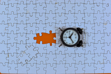 Alarm clock over missing puzzle piece suggests urgency, highlighting time's role in completing tasks or solving unresolved problems.の写真素材