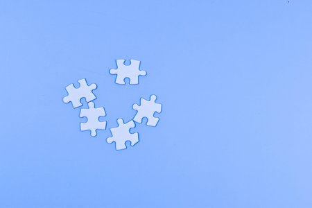 Scattered puzzle pieces on blue surface suggest individuality, separation, and the interplay between...