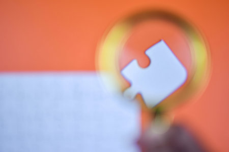 Magnifying glass enlarges white puzzle piece on orange background, emphasizing detail, fit, and...