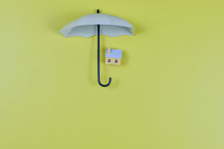 Large umbrella shelters two toy houses on yellow background, symbolizing home protection, safety, and the concept of insurance coverage.の写真素材