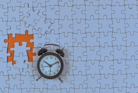 Alarm clock over missing puzzle piece suggests urgency, highlighting time's role in completing tasks...