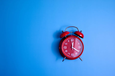 Red analog alarm clock on blue background highlights time awareness, urgency, and visual contrast in...