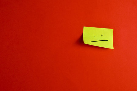 Yellow sticky note with sad face on red background.の写真素材