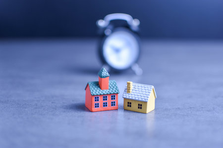 Two model houses with blurred clock in background suggest themes of home ownership, real estate timing, and housing-related decisions.の写真素材