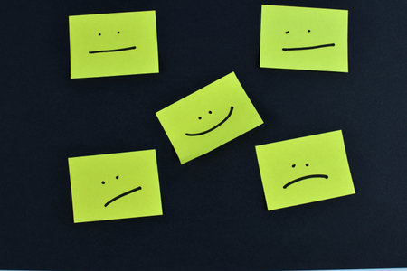 Nine yellow cards with varied facial expressions on dark background, illustrating a range of emotions through minimalistic design and layout.の写真素材