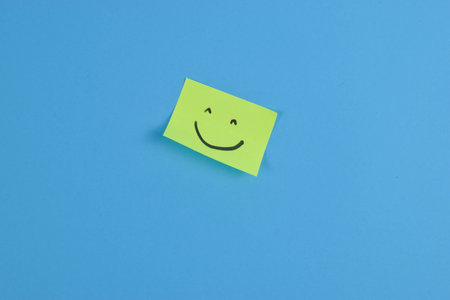 Green sticky note with cheerful smiley face on bright blue background, conveying positivity through bold color contrast and minimal design.の写真素材