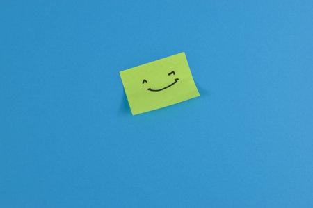 Green sticky note with cheerful smiley face on bright blue background, conveying positivity through bold color contrast and minimal design.の写真素材