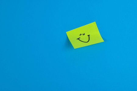 Yellow sticky note with cheerful smiley face on bright blue background, conveying positivity through bold color contrast and minimal design.の写真素材