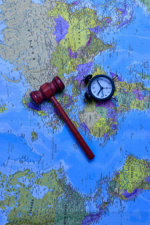 Red gavel and black stopwatch on world map symbolize global justice, legal urgency, and international decision-making across geographic boundaries.の写真素材