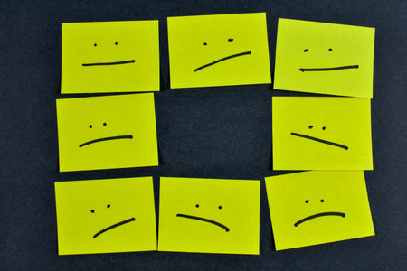Nine yellow cards with varied facial expressions on dark background, illustrating a range of emotions through minimalistic design and layout.の写真素材