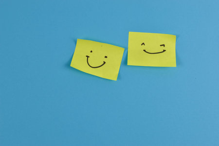 Yellow sticky note with cheerful smiley face on bright blue background, conveying positivity through...
