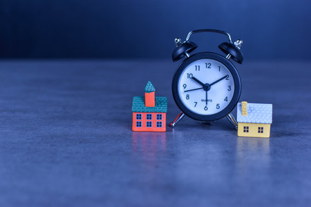 Two model houses with blurred clock in background suggest themes of home ownership, real estate timing, and housing-related decisions.の写真素材