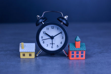 Two model houses with blurred clock in background suggest themes of home ownership, real estate timing, and housing-related decisions.の写真素材