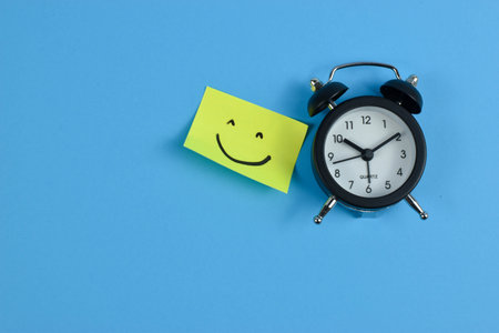Alarm clock and sticky note with smiley face on blue backgroundの写真素材