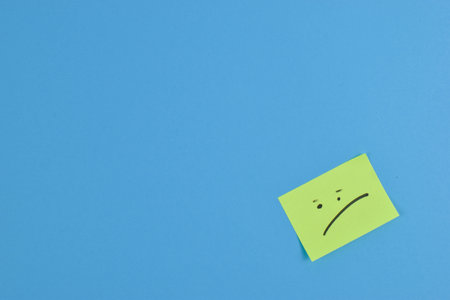 Yellow sticky note with a sad face on a blue background.の写真素材