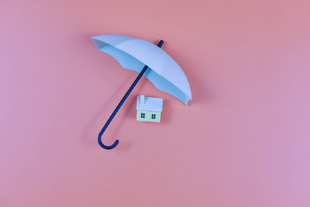 White umbrella and house on pink background combine symbols of protection in a minimalist, visually striking composition.の写真素材