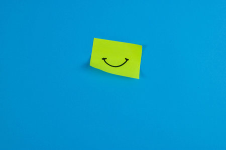 Yellow sticky note with cheerful smiley face on bright blue background, conveying positivity through...