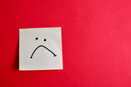 Sticky note with a frown face on red background, conveying a sense of disappointment or dissatisfaction through a simple and minimal design.の写真素材