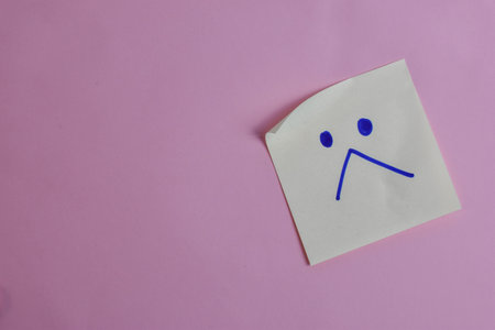 Light blue sticky note with sad face on pink background, expressing emotion through minimal design and strong visual contrast.の写真素材