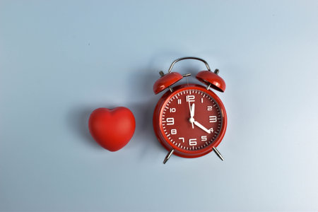 Red heart and black alarm clock on blue symbolic pairing suggesting loveâs connection to time, urgency, or enduring emotional presence.の写真素材
