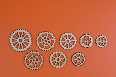 Eleven wooden gears on orange background, showcasing mechanical diversity through varied sizes, tooth counts, and spoke designs in organized layout.の写真素材