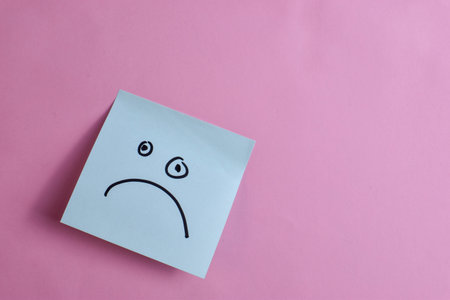 Light blue sticky note with sad face on pink background, expressing emotion through minimal design and strong visual contrast.の写真素材