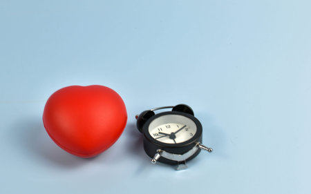Red heart and black alarm clock on blue symbolic pairing suggesting loveâ€™s connection to...
