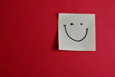 Yellow sticky note with smiley face on red background, conveying happiness and simplicity through...