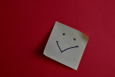 Sticky note with smiley face on red background, conveying happiness and simplicity through bold color contrast and minimal design.の写真素材