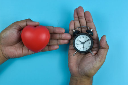 Red heart and black clock on blue surface highlight emotional care and time role in wellbeing.