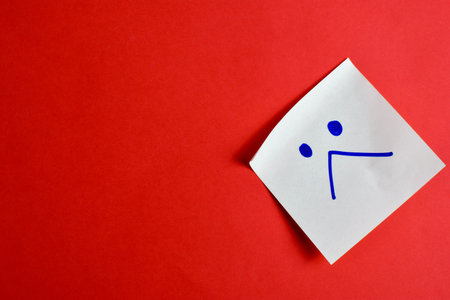 Sticky note with a face drawing on red background, conveying a message through bold color contrast and minimal design.の写真素材