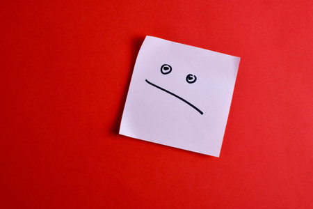 White sticky note with a frown face on red background, conveying simplicity through bold color contrast and minimal design.の写真素材