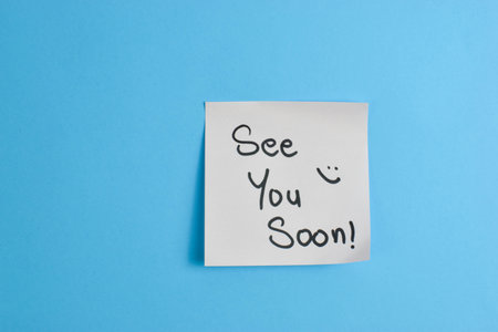 Yellow sticky note with See You Soon message on blue background, conveying warmth and greeting through simple text and strong color contrast.の写真素材