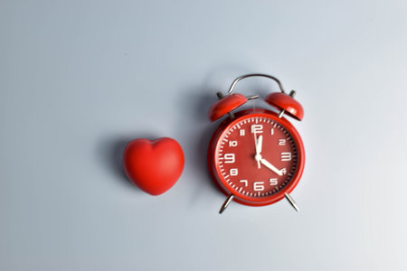 Red heart and black alarm clock on blue symbolic pairing suggesting loveâs connection to time, urgency, or enduring emotional presence.の写真素材
