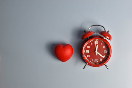 Red heart and black alarm clock on blue symbolic pairing suggesting loveâs connection to time, urgency, or enduring emotional presence.の写真素材