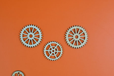 Four wooden gears on orange background, showcasing mechanical diversity through varied sizes, tooth counts, and spoke designs in organized layout.の写真素材