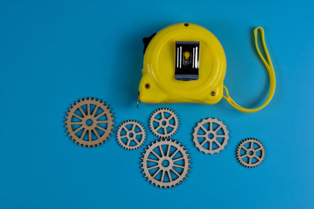 Yellow tape measure and six wooden gears on blue surface represent precision, measurement, and mechanical design in engineering or construction contexts.の写真素材