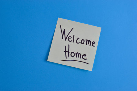 Yellow sticky note with Welcome Home message on blue background, conveying warmth and greeting through simple text and strong color contrast.の写真素材