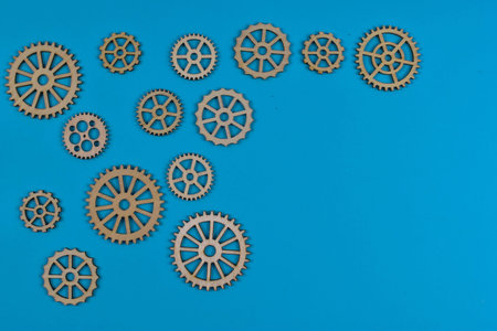 Eight wooden gears on blue surface illustrate mechanical interconnectivity, motion transfer, and...