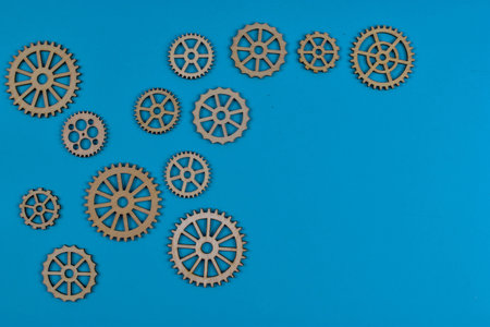 Eight wooden gears on blue surface illustrate mechanical interconnectivity, motion transfer, and design variation in engineering systems.の写真素材
