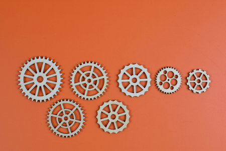 Eleven wooden gears on orange background, showcasing mechanical diversity through varied sizes, tooth counts, and spoke designs in organized layout.の写真素材
