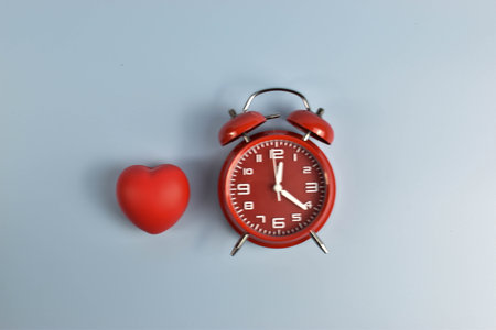 Red heart and black alarm clock on blue symbolic pairing suggesting loves connection to time, urgency, or enduring emotional presence.の写真素材