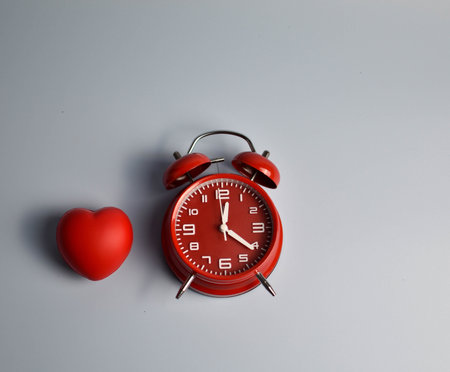 Red heart and black alarm clock on blue symbolic pairing suggesting loveâs connection to time, urgency, or enduring emotional presence.の写真素材