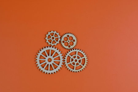 Four wooden gears on orange background, showcasing mechanical diversity through varied sizes, tooth...