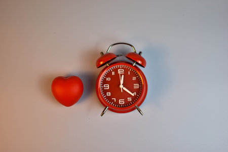 Red heart and black alarm clock on blue symbolic pairing suggesting loves connection to time, urgency, or enduring emotional presence.の写真素材