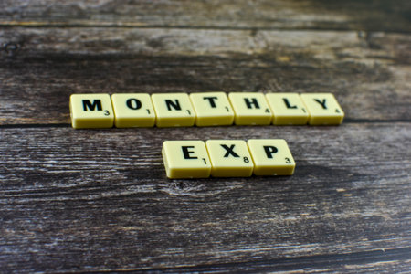 Scrabble tiles spell Monthly Exp on wood, suggesting abbreviated reference to monthly expenses in financial tracking or budgeting contexts.の写真素材